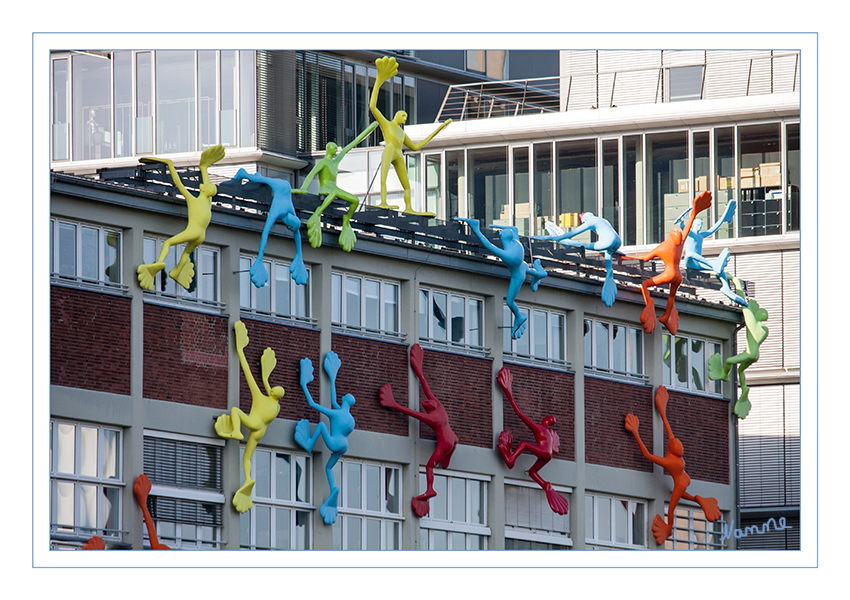 Flossis
1998, anlässlich der Eröffnung des Deutschen Kunststoff-Museums im NRW-Forum am Rhein und der Ausstellung "Kunst und Kunststoff", hatten die von der Künstlerin Rosalie entworfen Kletterer ihren ersten großen Auftritt in Düsseldorf. Die gelben, grünen, roten und blauen Figuren krabbelten auf die Fassade des NRW-Forums Kultur und Wirtschaft und hangelten sich bis zum Dach empor – bis der Denkmalschutz den Krabbelausflug - zunächst - beendete.  Im März 2002 durften die Flossis, von der Unternehmensgruppe Klüh als Schenkung für die Stadt erworben, den Medienhafen erobern. 24 Figuren sind dort am Roggendorf-Speicher heimisch geworden. Fünf weitere klettern am Nachbargebäude. Die Installation der bis zu 4,2 Meter hohen und 2,5 Meter breiten Skulpturen umfasst damit ein Gesamtensemble von 29 Figuren, die sich über eine Fassadenfläche von rund 800 Quadratmeter verteilen. Jede der Figuren ist ein Unikat, differenziert in unterschiedlicher Haltung und formaler Gestaltung.
Schlüsselwörter: Düsseldorf; Medienhafen; Flossis; Roggendorf-Haus