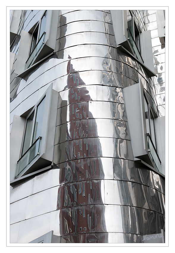 Neuer Zollhof 2
Der  siebengeschossige  „Neue  Zollhof  2“  spiegelt  mit  seiner  Edelstahlfassade  in  der  Mitte  des  skulptural  wirkenden  Ensembles  die  beiden höheren Nachbarhäuser wieder. laut aknw.de
Schlüsselwörter: Düsseldorf; Medienhafen; Neuer Zollhof;