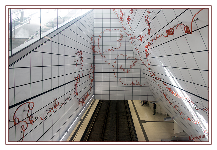 U-Bahnhof und Kunst - Kirchplatz -
Düsseldorf
Am „Kirchplatz“ begleitet die Leipziger Künstlerin Enne Haehnle die Fahrgäste mit einem eigenen Textfragment bis zum Gleis. Die Worte sind leuchtend farbig und scheinen auf die weißen Fliesen montiert durch die Station zu schweben. Die Schriftzüge wurden geschmiedet, teilweise erinnern sie an plastische Wortknäuel. laut wz.de
Schlüsselwörter: Düsseldorf, U-Bahn, Bahnhof, Kunst