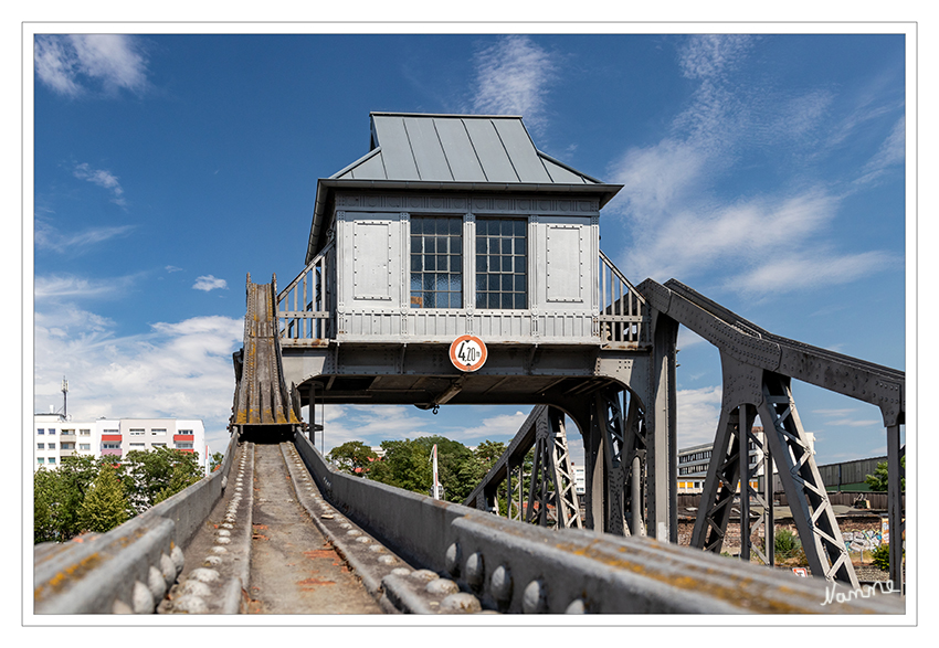 Kölntour - Deutzer Drehbrücke
Sie wurde 1907 zeitgleich mit dem Bau des Deutzer Hafens errichtet und im März 1908 dem Verkehr übergeben. Das technische Denkmal besteht aus einer genieteten Stahlfachwerkkonstruktion einer ungleichschenklig ausbalancierten Brücke von 31,29 Meter Spannweite und 10 Meter Breite, die aus dem bis heute vollständig erhaltenen Steuerhäuschen aus Stahlblech über der Brückenmitte elektrisch gesteuert werden kann. Geländer, Brückenköpfe und Steuerhaus wurden im geometrischen Jugendstil gestaltet.
laut Wikipedia
Schlüsselwörter: Köln; Deutzer Drehbrücke