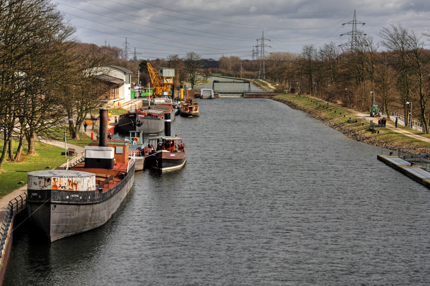 Blick vom Schiffshebewerk auf das Oberwasser
Auf einem 400 m langen Kanalabschnitt im Anschluss an den oberen Vorhafen zeigt das Museum eine Sammlung historischer Schiffe und schwimmender Arbeitsgeräte, eine Anlege- und Verladestelle für Güterschiffe, eine Hellinganlage zur Schiffsreparatur mit historischem Drehkran von 1906 und den Kanaldurchlass mit altem Klapptor von 1914 sowie eine historische Hubbrücke von 1897.
Schlüsselwörter: Henrichenburg       Schiffshebewerk