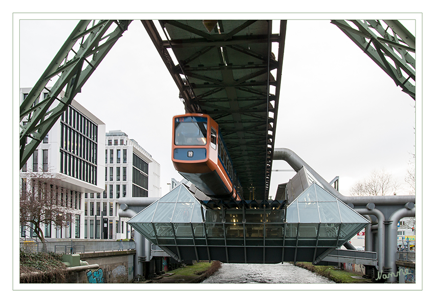 Wuppertal - Schwebebahn
Am 4. September 1982 konnte die bereits 1974 vom Architekturbüro Rathke entworfene Station unter dem neuen Namen „Ohligsmühle“ eröffnet werden. Beim Ausbau wurde die Station saniert, der Austausch der Tragkonstruktion konnte erfolgen, da die Station selbst nicht vom Gerüst der Schwebebahn getragen wird. Bei der Sanierung wurde die ursprünglich türkis gefärbte Verglasung durch eine neutrale ersetzt. Die mehrfach gekröpften meterdicken Rohre, die die Station tragen, wurden von Rot in Silber umlackiert. Die Rolltreppen wurden entfernt und durch zwei Aufzüge ersetzt. Sie ist die einzige Station der Strecke mit prismenförmigen Aufgänge und Bahnsteigen und erschließt die westliche Innenstadt Elberfelds.
Schlüsselwörter: Wuppertal; Schwebebahn; Ohlingsmühle