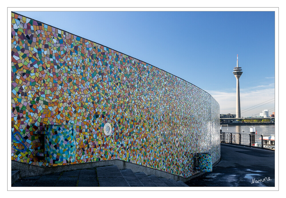 Burgplatztreppe
Fröhlich ist die Kunst, die der Kunstakademie-Professor Hermann-Josef Kuhna uns Düsseldorfer und dem Rest der Welt schenkte
Sein größtes Kunstwerk in Düsseldorf sind die Wände der Treppe und des Abgangs, die den Burgplatz in der Altstadt mit dem Rheinufer verbinden. Ursprünglich war das 320 Quadratmeter große Werk „Rivertime“ ein Wandgemälde, ein „Mural“ im besten Street-Art-Sinne. 2017 wurde es als Fliesen-Mosaik runderneuert. laut Wikipedia
