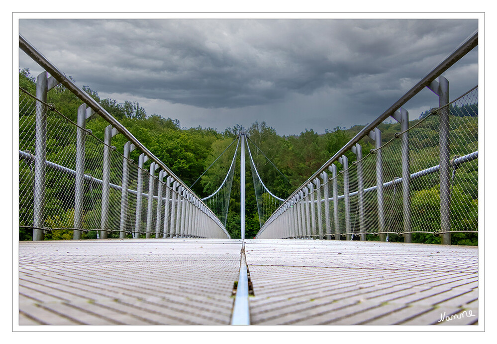 Kleine Eifeltour - Victor Neels Brücke
Zunächst wurde am östlichen Seeufer ein rd. 20 Meter hoher, mit 17° zum Berghang geneigter und mit zwei Seilen abgespannter Stahl-Pylon errichtet. Zwischen diesem und zwei Stahlbetonscheiben am Westufer (Brüstung) wurden zwei Tragseile gespannt; darunter liegen zwei Spannseile. Insoweit besteht die gesamte Tragkonstruktion im Wesentlichen nur aus vier Seilen. Der durch Stahlgeländer mit Drahtverkleidung gesicherte Überweg mit Aluminiumbelag ist behindertengerecht gebaut. laut Wikipedia
Schlüsselwörter: Eifel