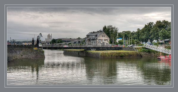 Deutzer Drehbrücke
wurde 1907 errichtet und im März 1908 dem Verkehr übergeben. Das technische Denkmal besteht aus einer genieteten Stahlfachwerkkonstruktion einer ungleichschenklig ausbalancierten Brücke von 31,29 m Spannweite und 10 m Breite, die aus dem bis heute vollständig erhaltenen Steuerhäuschen aus Stahlblech über der Brückenmitte elektrisch gesteuert werden kann.
Schlüsselwörter: Deutzer              Drehbrücke                    Köln