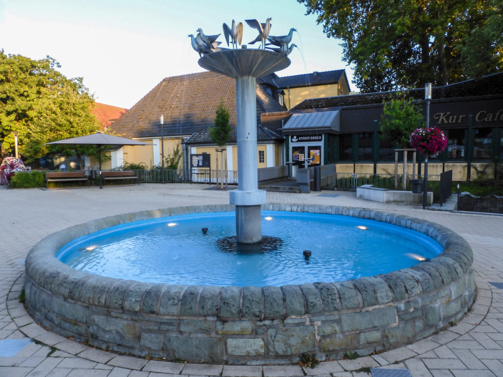 Der Vogelbrunnen
ist ein wahrer Hingucker. Er gleicht einer großen Vogeltränke. Zehn Tauben haben sich oben niedergelassen, um sich mit dem kühlen Wasser zu erfrischen. Eingefasst ist der Brunnen in den für die Gegend typischen Grünsandstein. (badsassendorf.de)
Schlüsselwörter: 2026